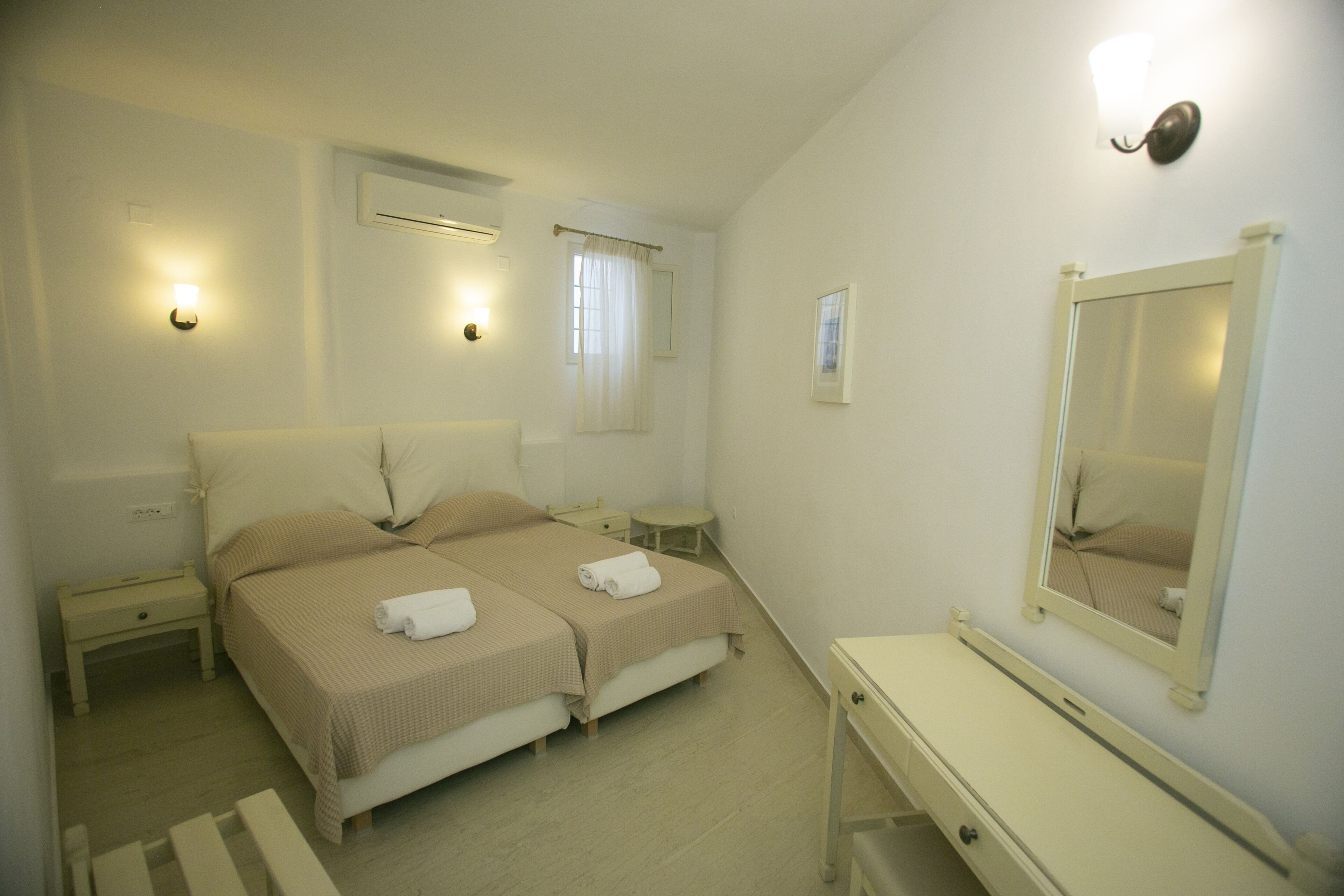 Une chambre avec deux lits, une table de chevet, une commode, un miroir et une fenêtre avec des rideaux.