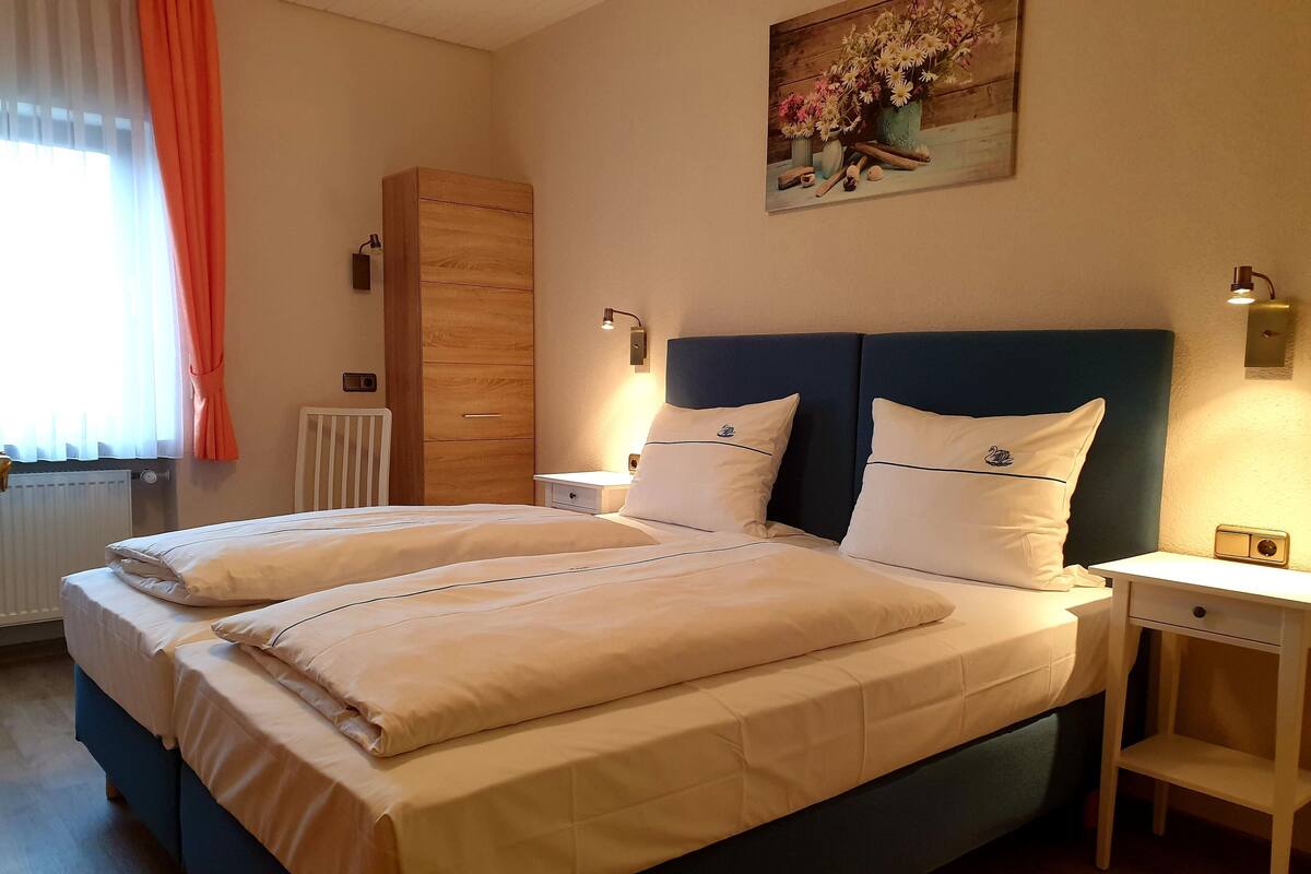 A double bed with a wooden headboard, two bedside tables, a nightstand, and a painting on the wall.