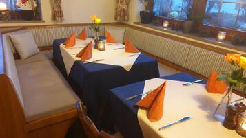 Un comedor con mesas dispuestas para cuatro, cada una con servilletas anaranjadas, un florero con una flor amarilla y una vela.
