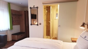 A hotel room with a bed, a wooden wardrobe, a mirror, and a shower area. - Hotel Gasthof zum Schwan (Steinsfeld)