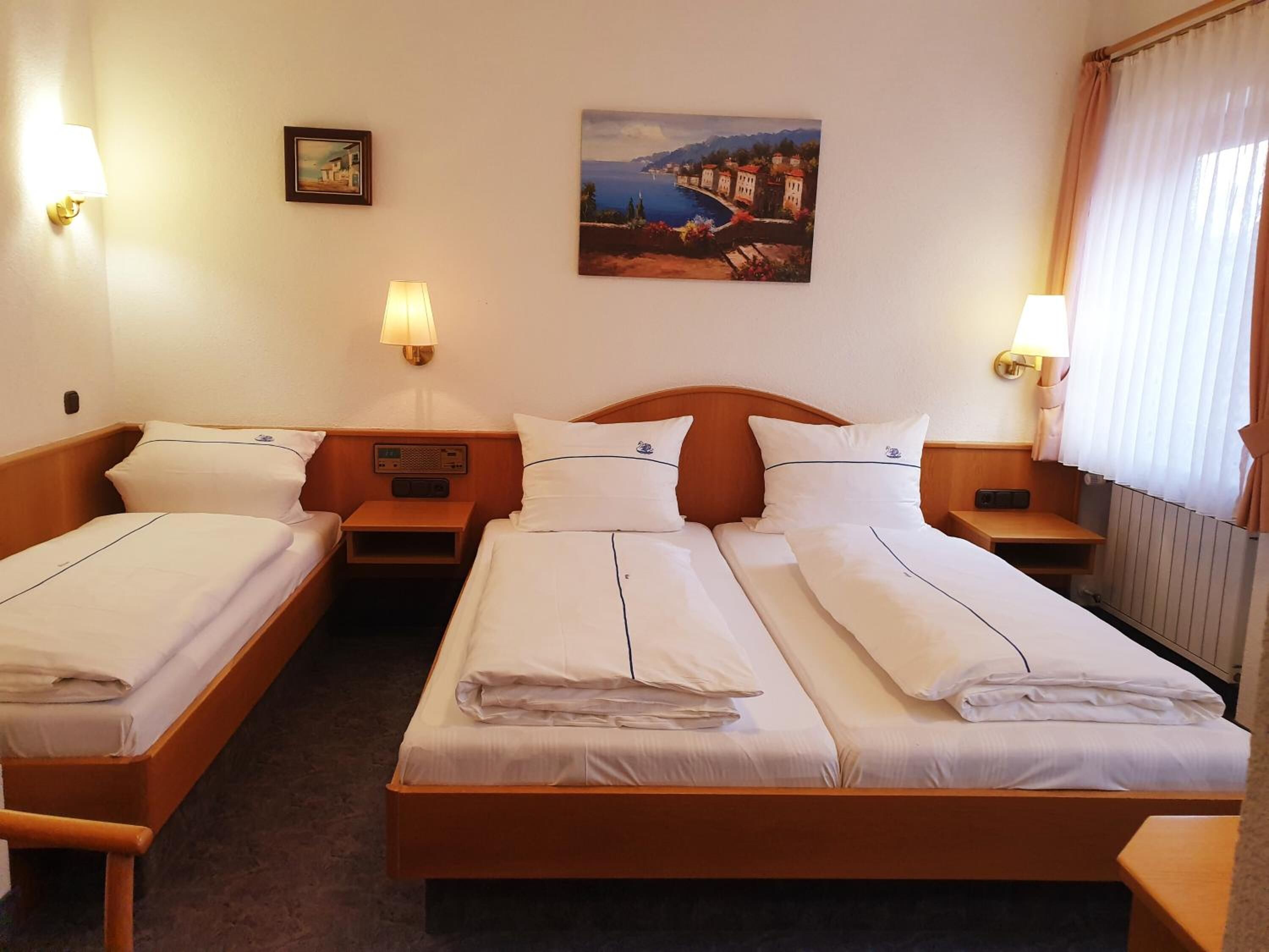 Una habitación de hotel con dos camas individuales, un cabecero de madera, mesitas de noche, una radio y un cuadro de una escena costera.