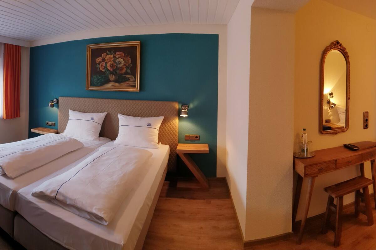 A hotel room with a bed, bedside table, desk, chair, and a mirror.