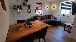A modern living room with a wooden dining table, black chairs, a brown sofa, and a small side table. - Hotel Gasthof zum Schwan (Steinsfeld)