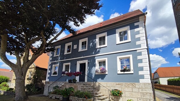 A two-story building with a stone facade and multiple windows, surrounded by a well-maintained garden and a tree. - Hotel Gasthof zum Schwan (Steinsfeld)