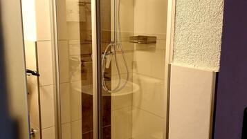 Een douchecabine met glazen wanden, een handdouche en een kraan op de muur.