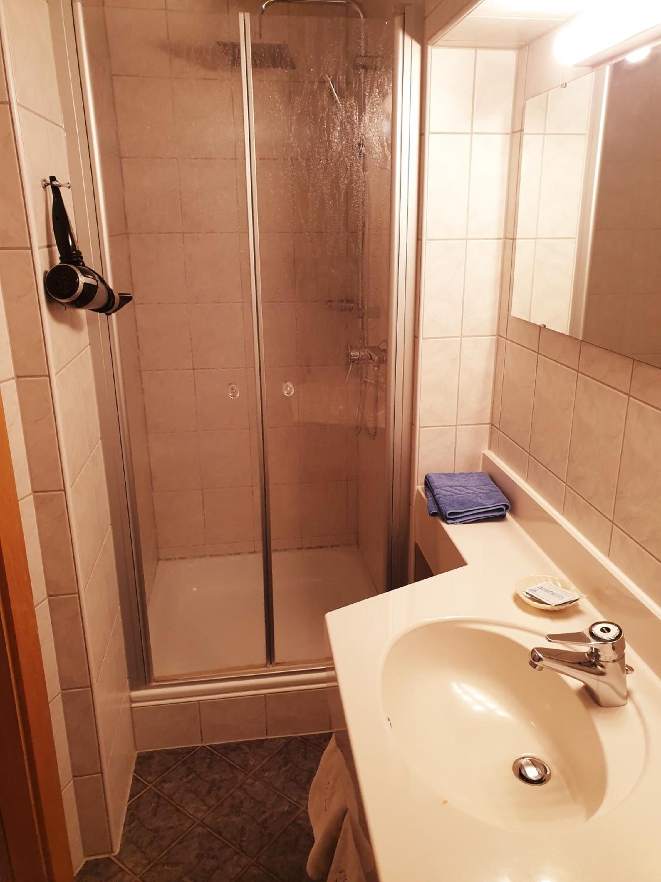 A bathroom with a glass shower enclosure, a sink with a mirror, and a towel rack.
