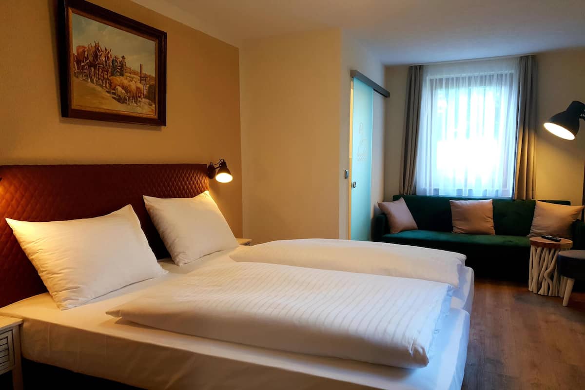 A hotel room with a large bed, a green sofa, a small table, and a painting on the wall.