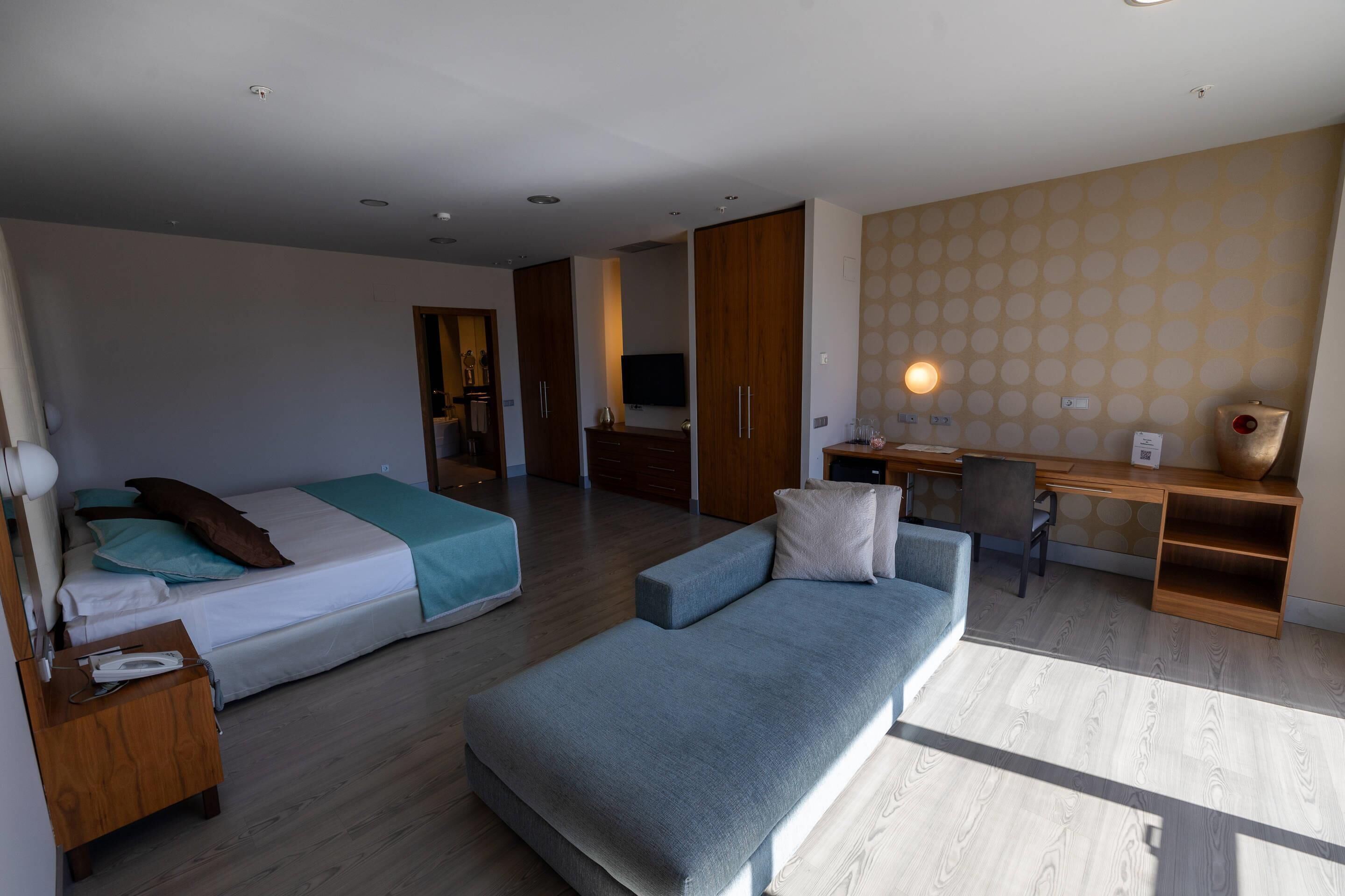 A modern hotel room with a bed, a sofa, a desk, and a TV.