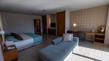 A modern hotel room with a bed, a sofa, a desk, and a TV.