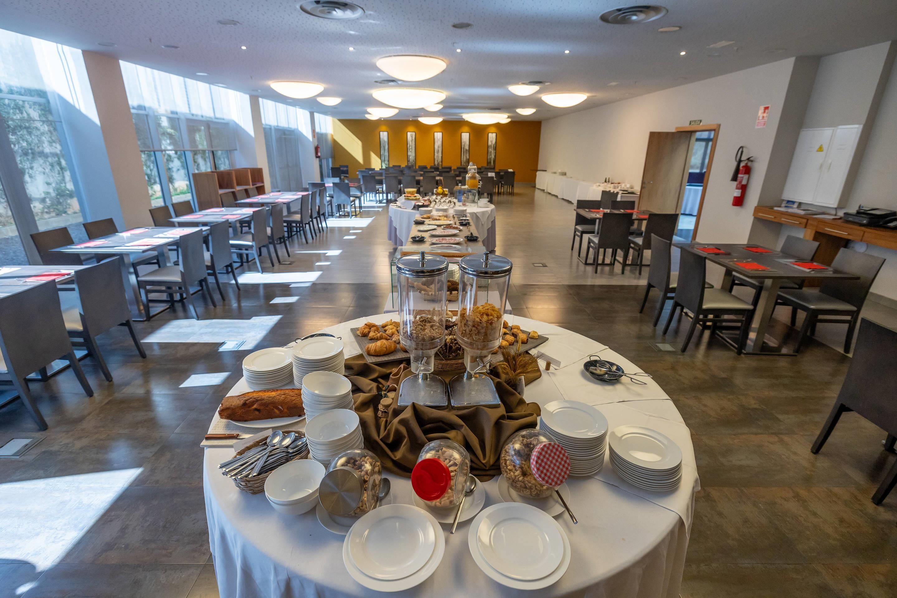 A spacious dining area with round tables set for breakfast, featuring various food items and utensils.