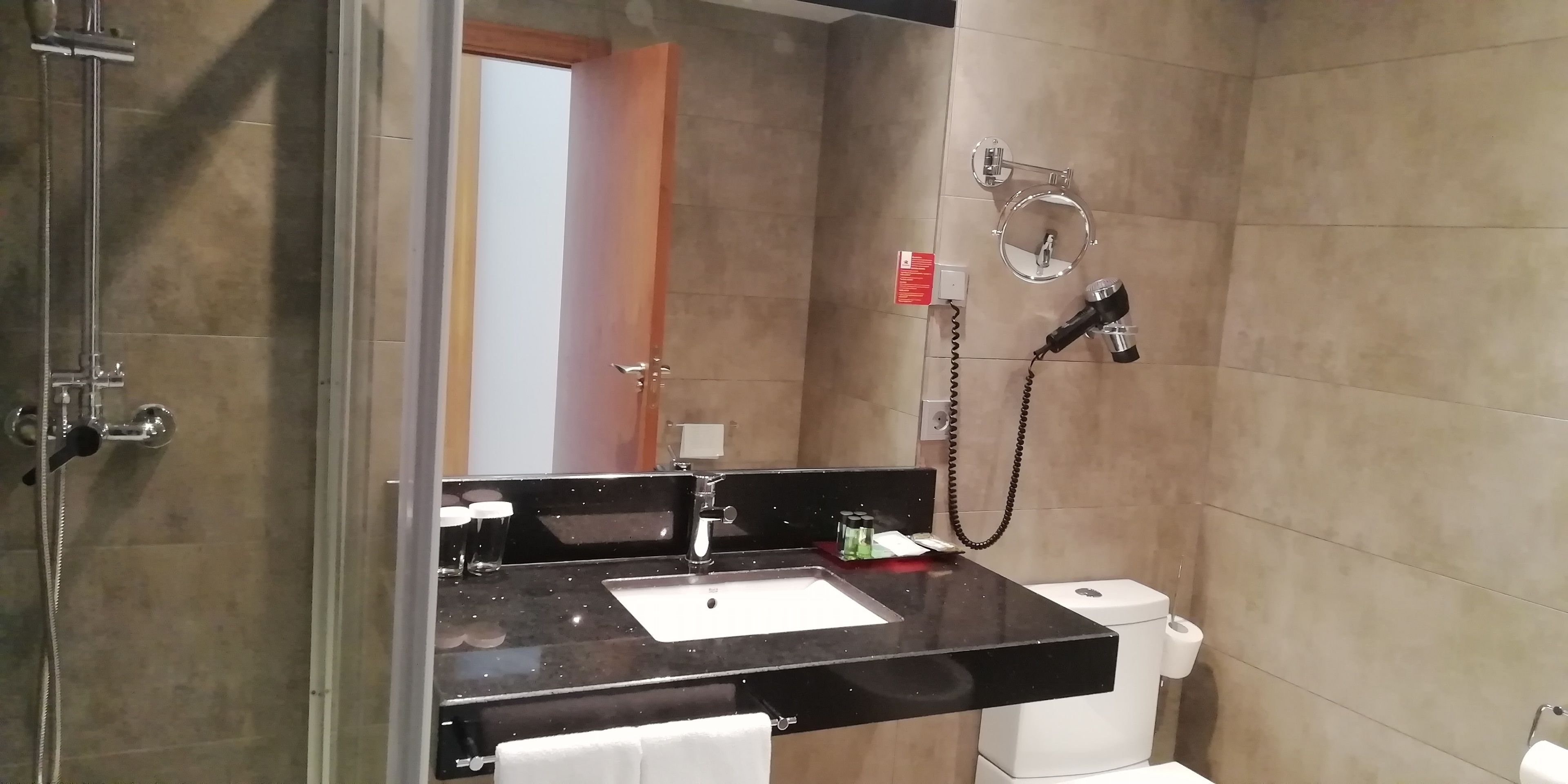 Un bany modern amb taulell negre, dutxa amb envàs de vidre, vàter i porta tovallons.
