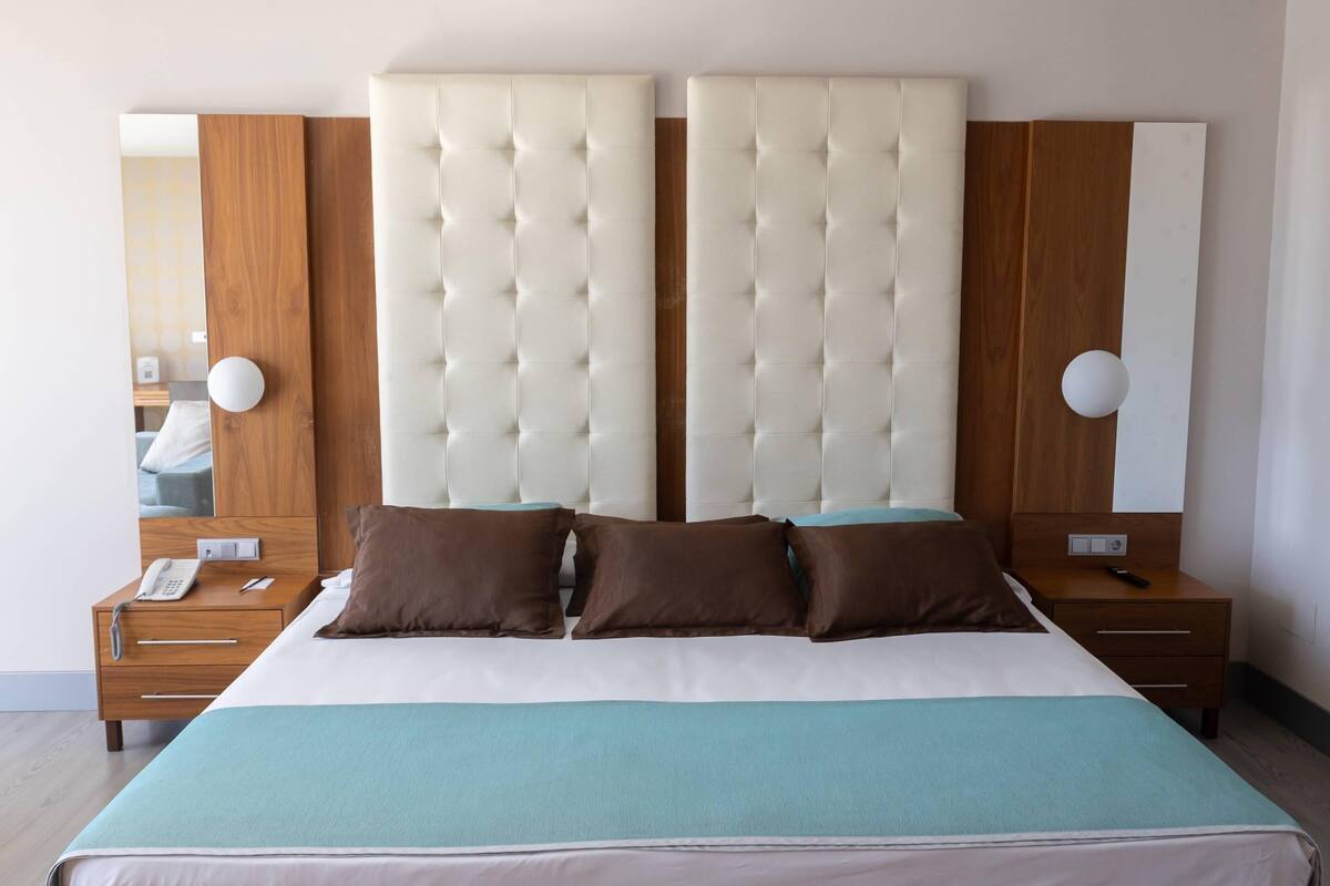 Habitación de hotel con una cama grande, dos mesitas de noche, un cabecero de madera y un espejo.