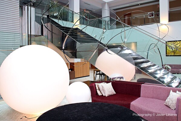 Un interior moderno con una escalera de cristal, un sofá rojo y una gran lámpara esférica blanca.