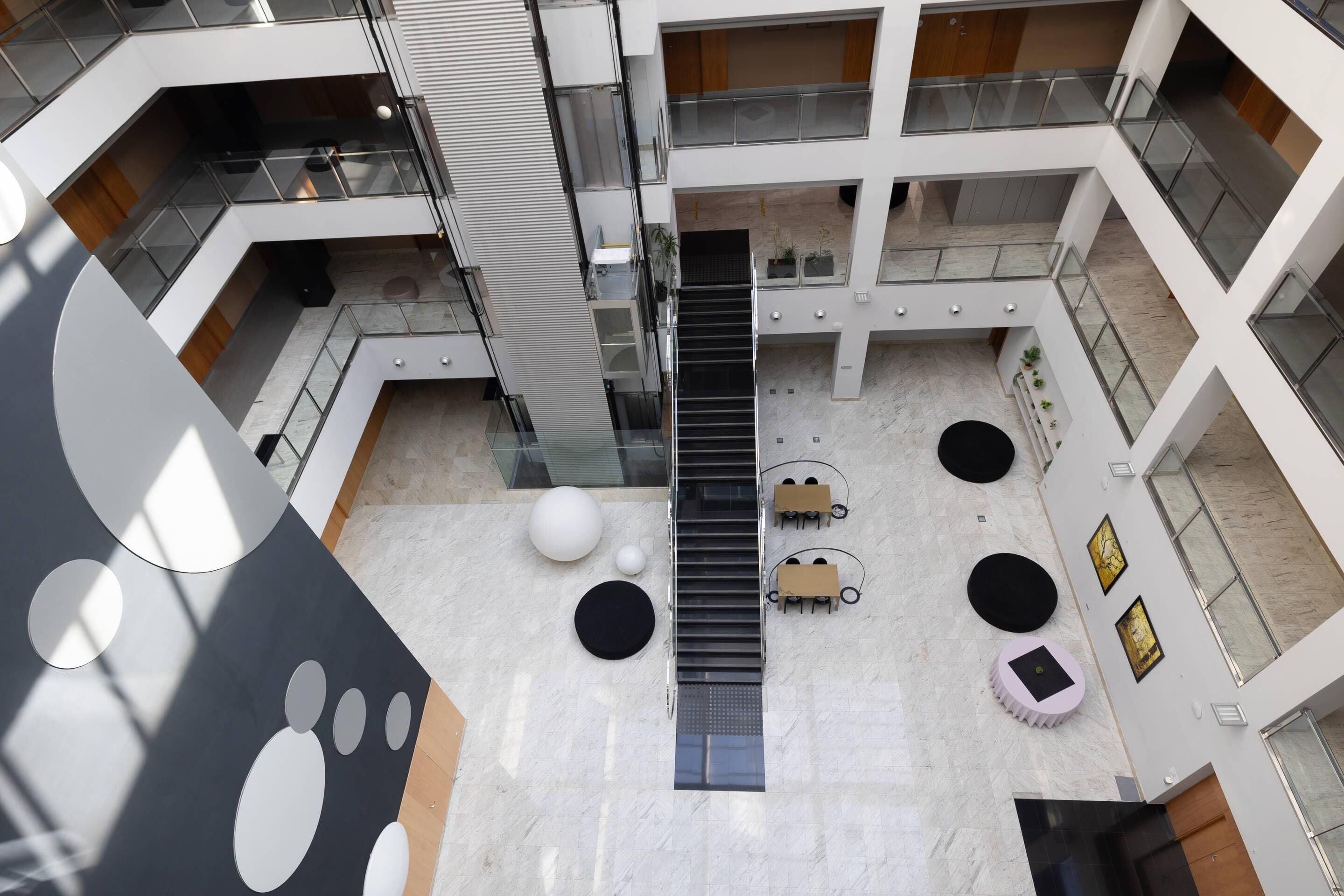 A multi-level atrium with a central staircase, seating areas, and a large abstract wall design.