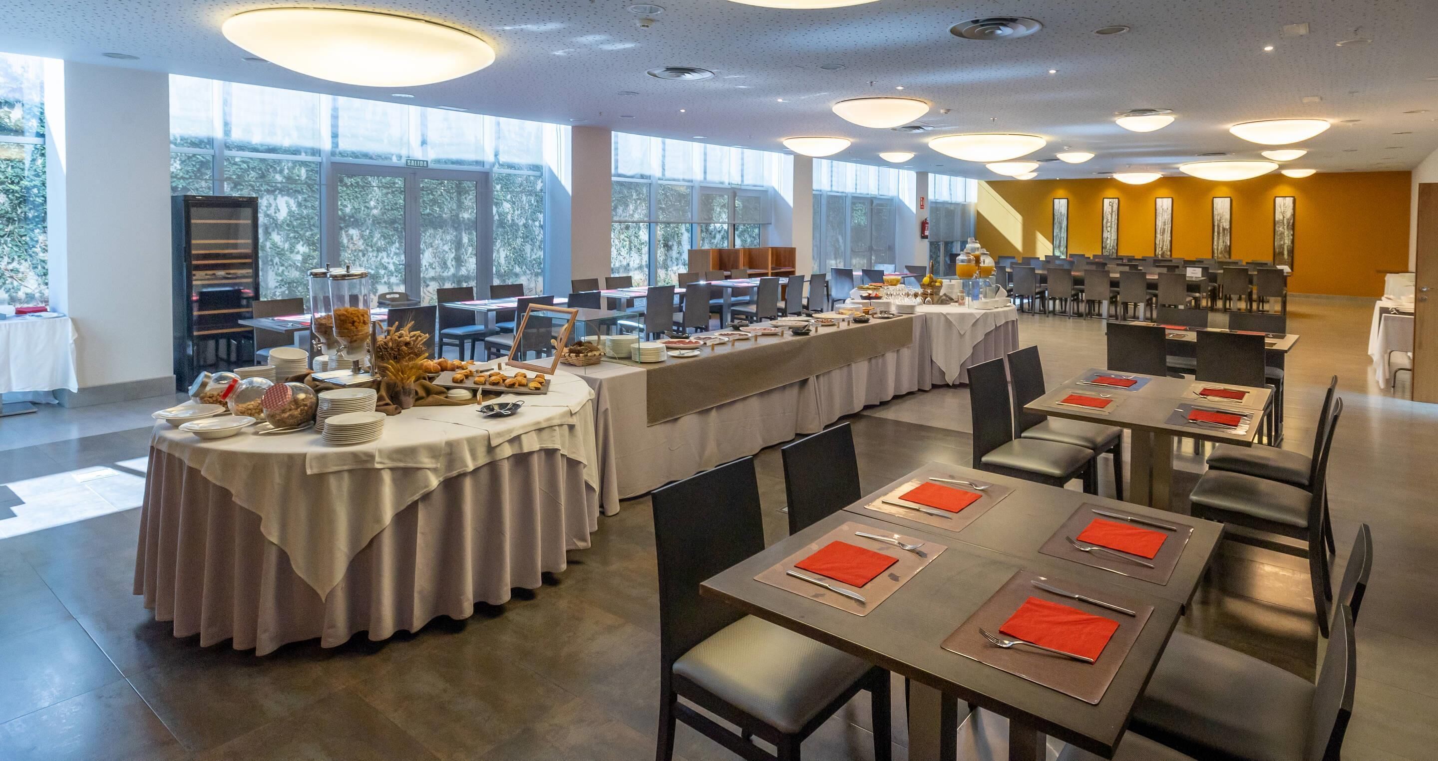 Un comedor amplio con varias mesas dispuestas para comidas, ventanas grandes que brindan luz natural y un diseño de interiores moderno.