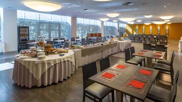Un comedor amplio con varias mesas dispuestas para comidas, ventanas grandes que brindan luz natural y un diseño de interiores moderno.