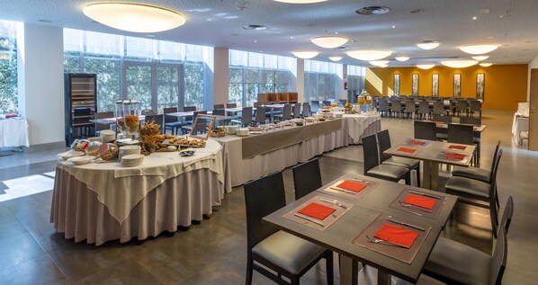 Un comedor amplio con varias mesas dispuestas para comidas, ventanas grandes que brindan luz natural y un diseño de interiores moderno.
