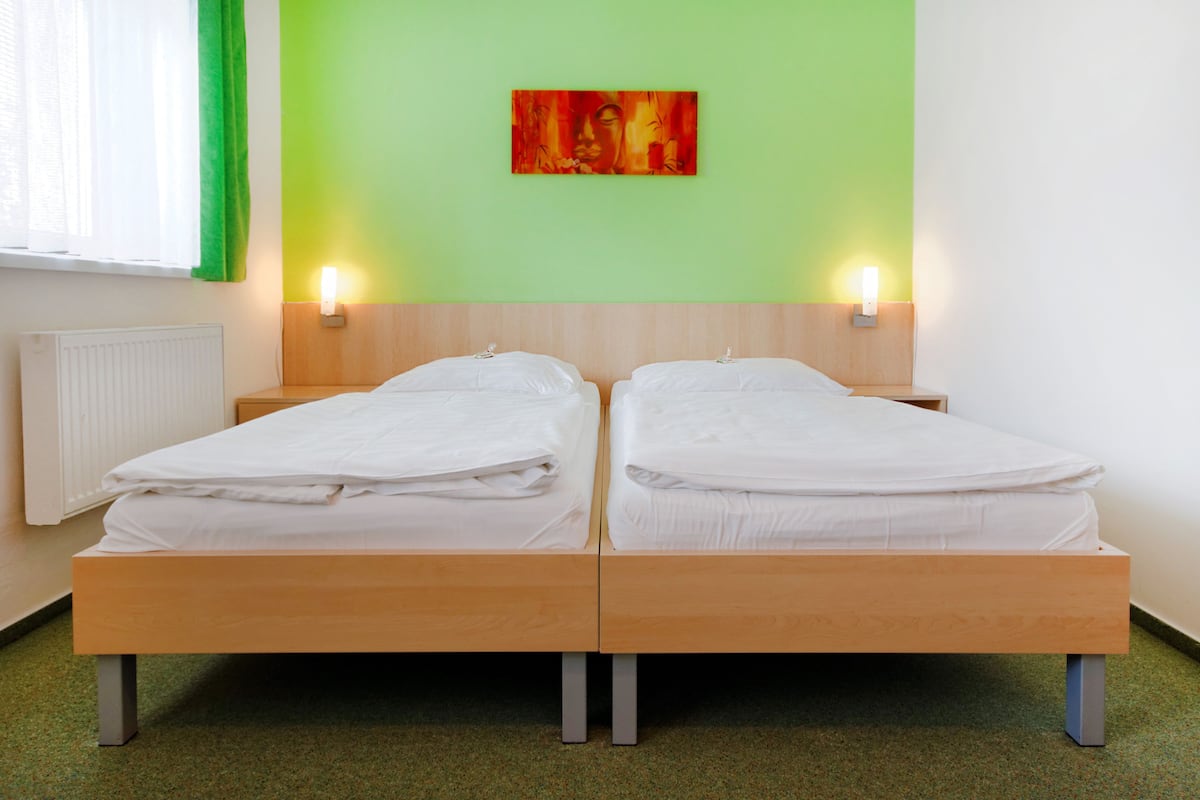 A double bed with two bedside tables, a green wall, and a painting.