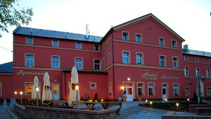 Un edificio rojo con letreros que indican 'Hotel Restaurant', mesas al aire libre y un camino de ladrillo que conduce a la entrada.