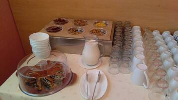 Montaje de un bufé de desayuno con diversas opciones de comida, una jarra de leche y múltiples vasos y platos.