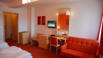 Une chambre d’hôtel équipée d’un lit, d’un bureau, d’une chaise, d’un canapé, d’une télévision et d’un miroir.