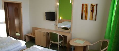 A hotel room with two beds, a desk with a chair, a small table, a TV, and artwork on the wall.