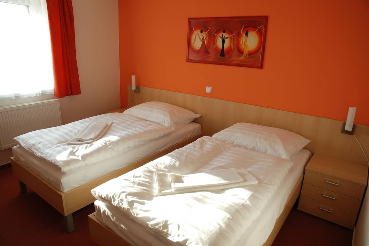 A room with two single beds, a wooden headboard, a nightstand with drawers, and a painting on the wall.