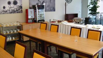 A conference room with a long table, chairs, a coffee machine, a clock, and a plant.