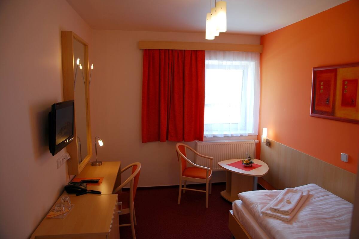 A hotel room with a bed, a desk with a chair, a TV, and a window with curtains.