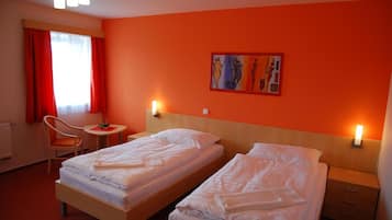Camera d'albergo con due letti, una poltrona, un tavolino e un quadro appeso al muro.