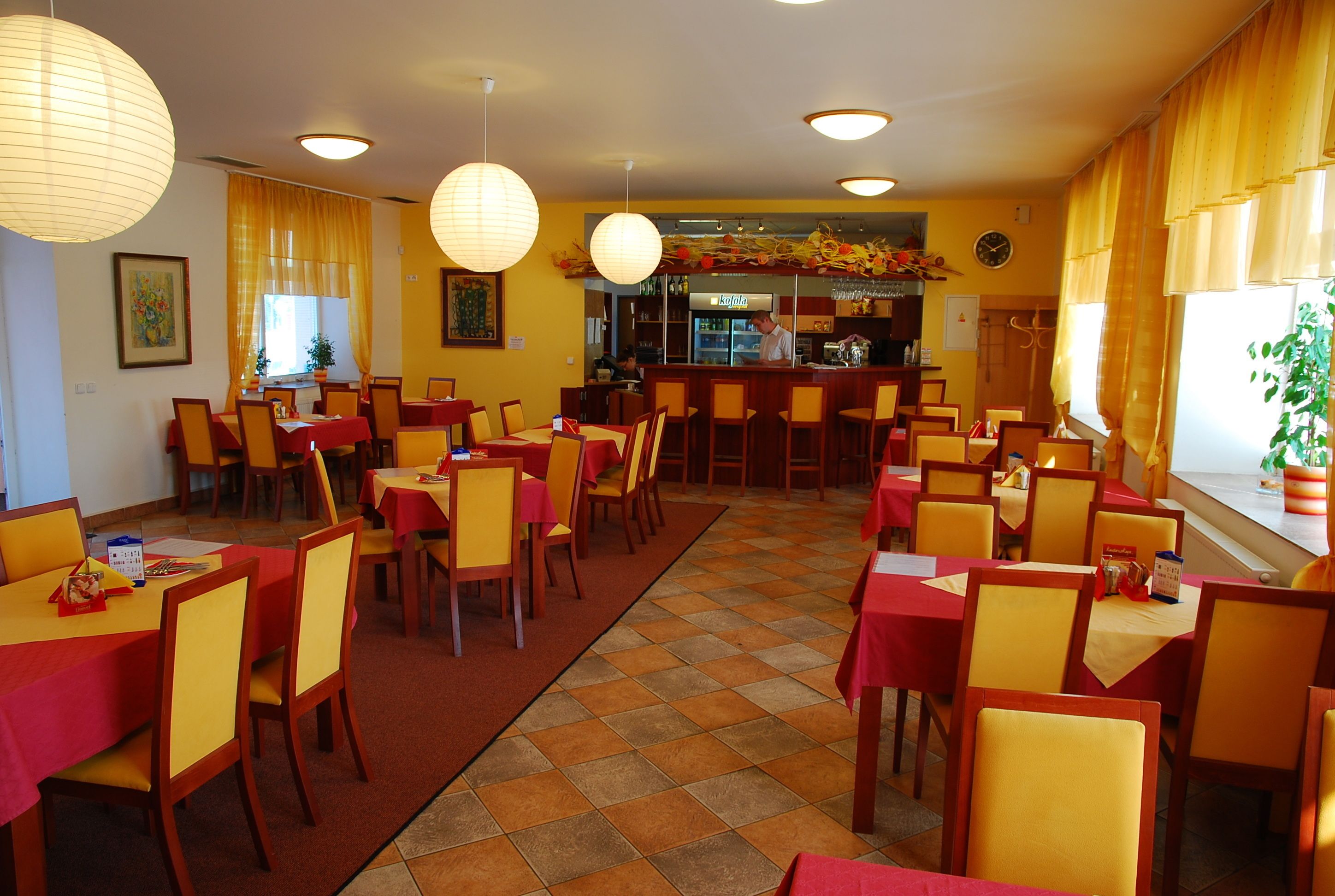 Un restaurante con varias mesas y sillas, una zona de bar y un reloj en la pared.