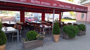 Un área de estar al aire libre del Hotel Senimo con mesas y sillas, rodeada de plantas en macetas.