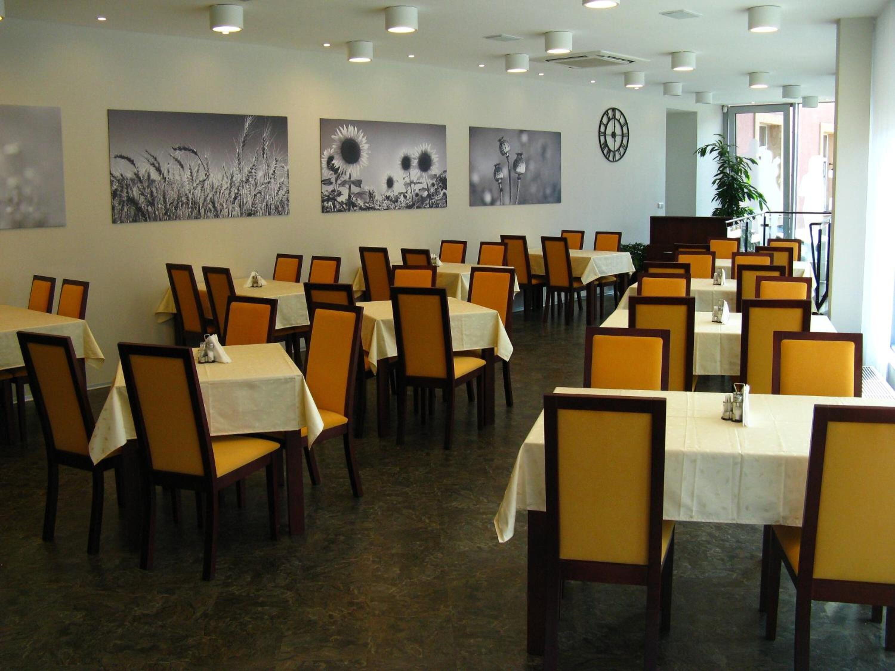 A dining area with tables and chairs, artwork on the walls, and a clock.