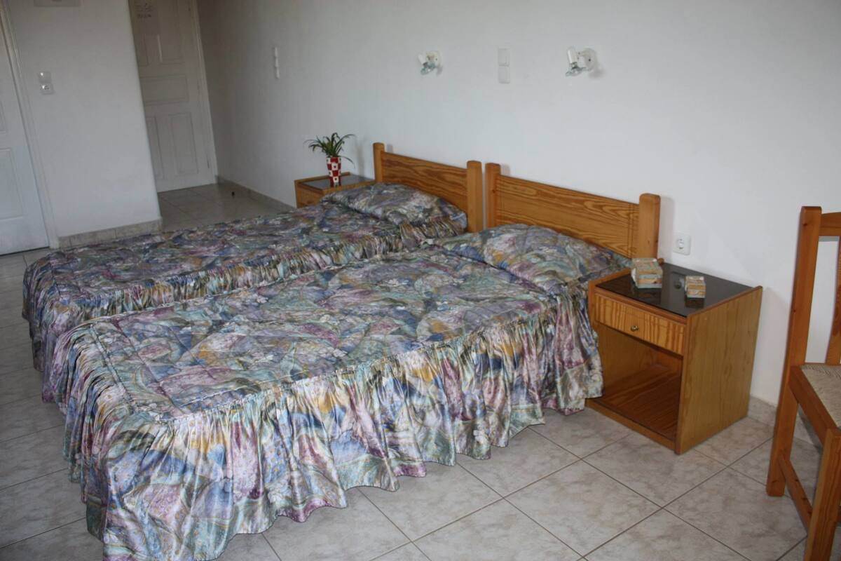 A bedroom with two beds, a nightstand, a wooden chair, and a small table with a lamp.