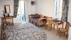 Une chambre avec un lit, un bureau et une chaise. Il y a une fenêtre avec des rideaux et une porte qui donne sur un espace extérieur.