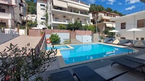 A pool area with lounge chairs and a lifebuoy, surrounded by buildings and greenery. - Christina Studios & Apartments (Parga)