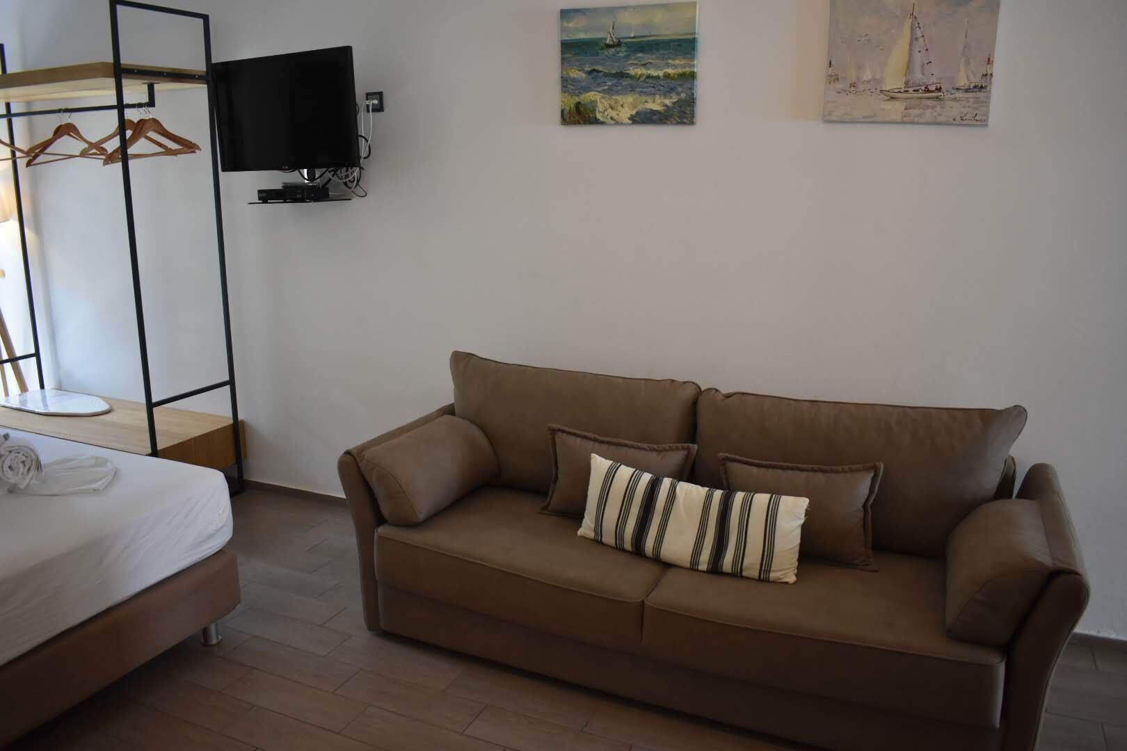Une pièce avec un canapé marron, un lit, un téléviseur fixé au mur et deux tableaux.