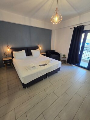 A modern hotel room with a large bed, bedside lamps, a small table, a chair, and a view of the outdoors. - Christina Studios & Apartments (Parga)