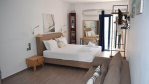 A modern bedroom with a large bed, a wooden nightstand, a sofa, a mirror, and a shelf with plants. - Christina Studios & Apartments (Parga)