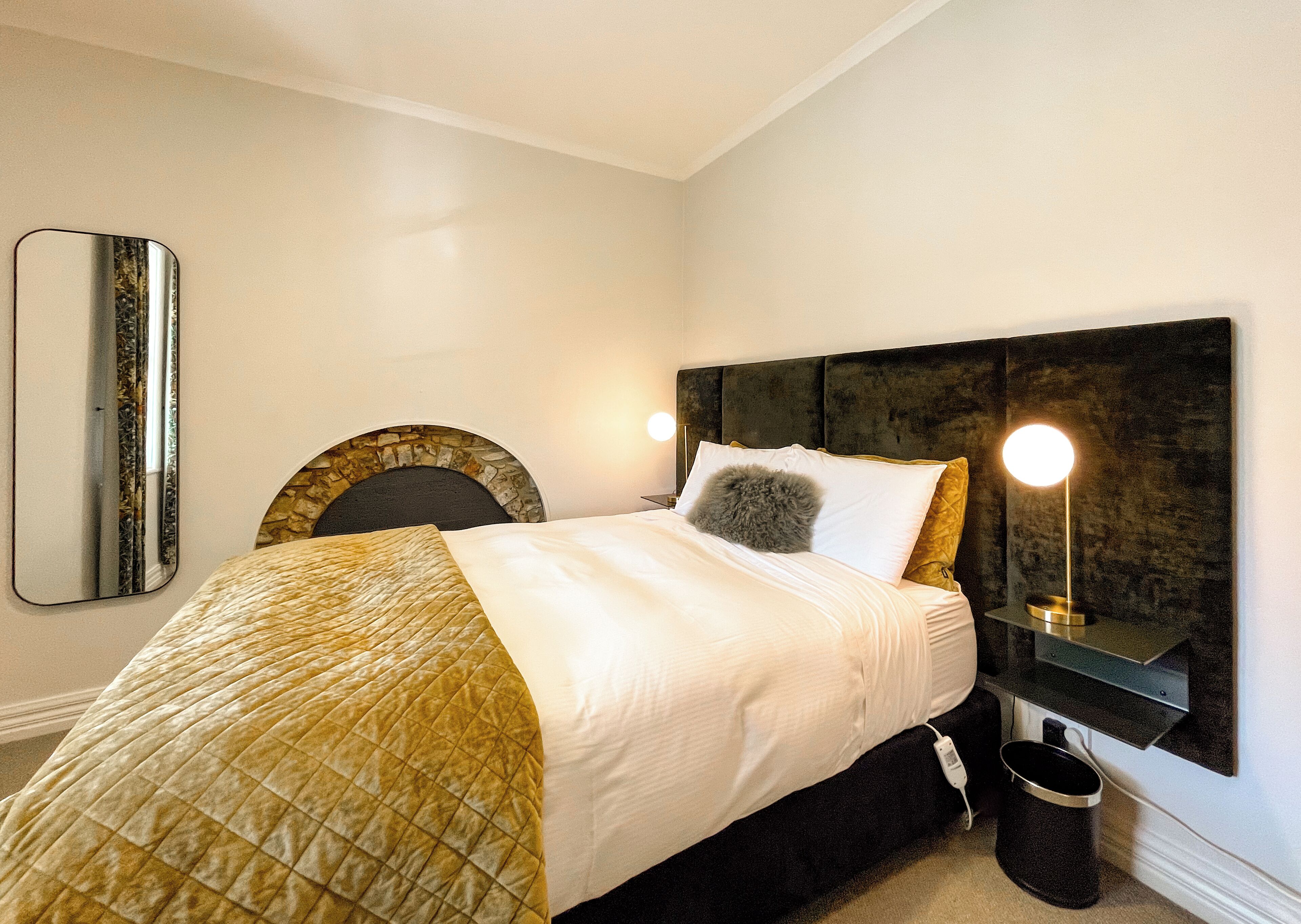 A neatly made bed with a quilted blanket, a round throw pillow, and a bedside lamp.