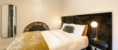 A neatly made bed with a quilted blanket, a round throw pillow, and a bedside lamp.