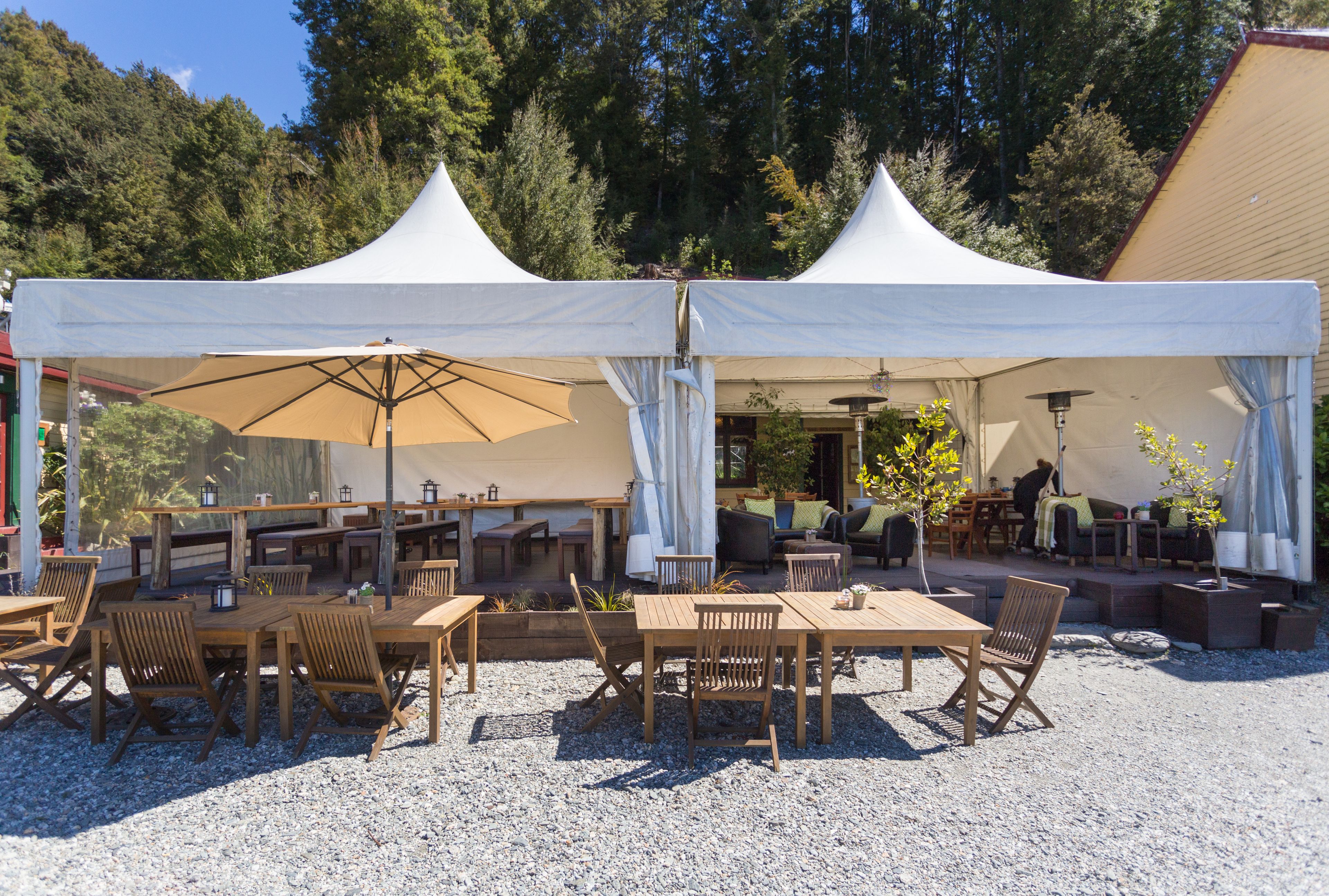 A covered outdoor seating area with tables and chairs, surrounded by trees.