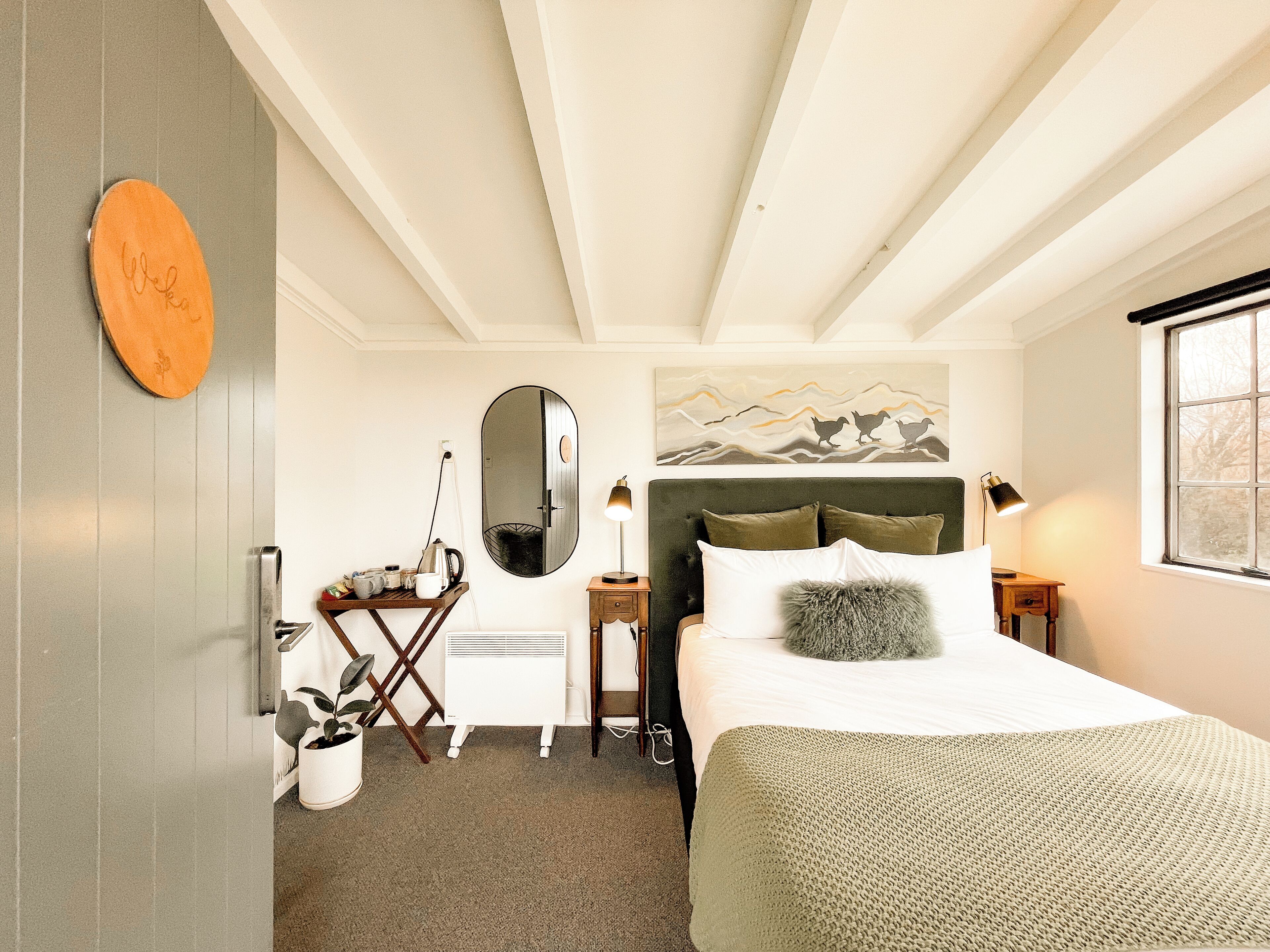 Una habitación de hotel con cama, escritorio, espejo, un cuadro y ventana.