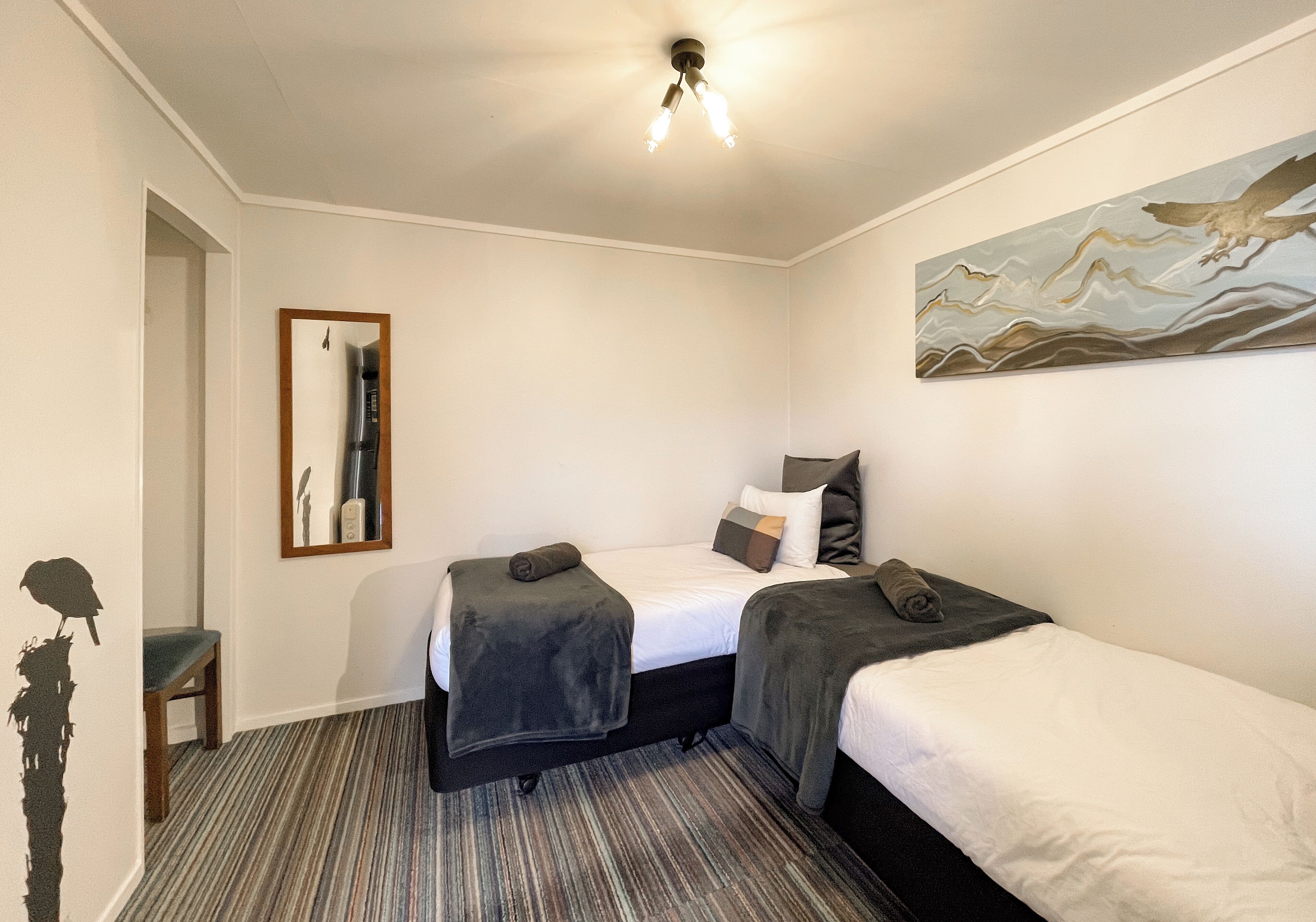 Een hotelkamer met twee bedden, een spiegel, een schilderij en een gestreept tapijt.