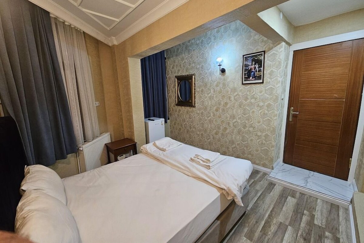 A hotel room with a bed, a small bedside table, a mirror, a picture on the wall, and a door.