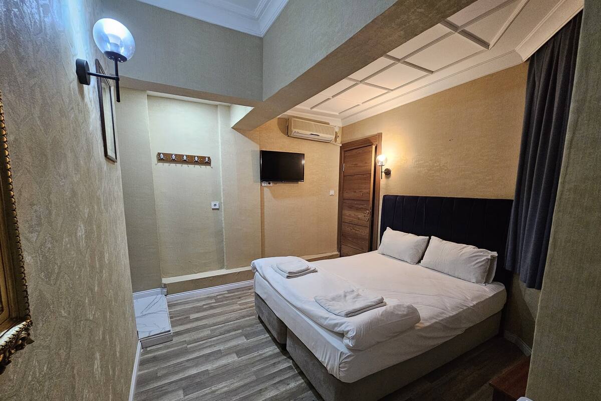 A hotel room with a bed, a TV, a wall-mounted air conditioner, and a wooden door.