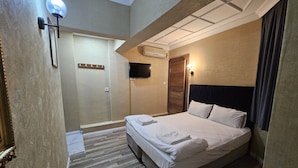 A hotel room with a bed, a TV, a wall-mounted air conditioner, and a wooden door.