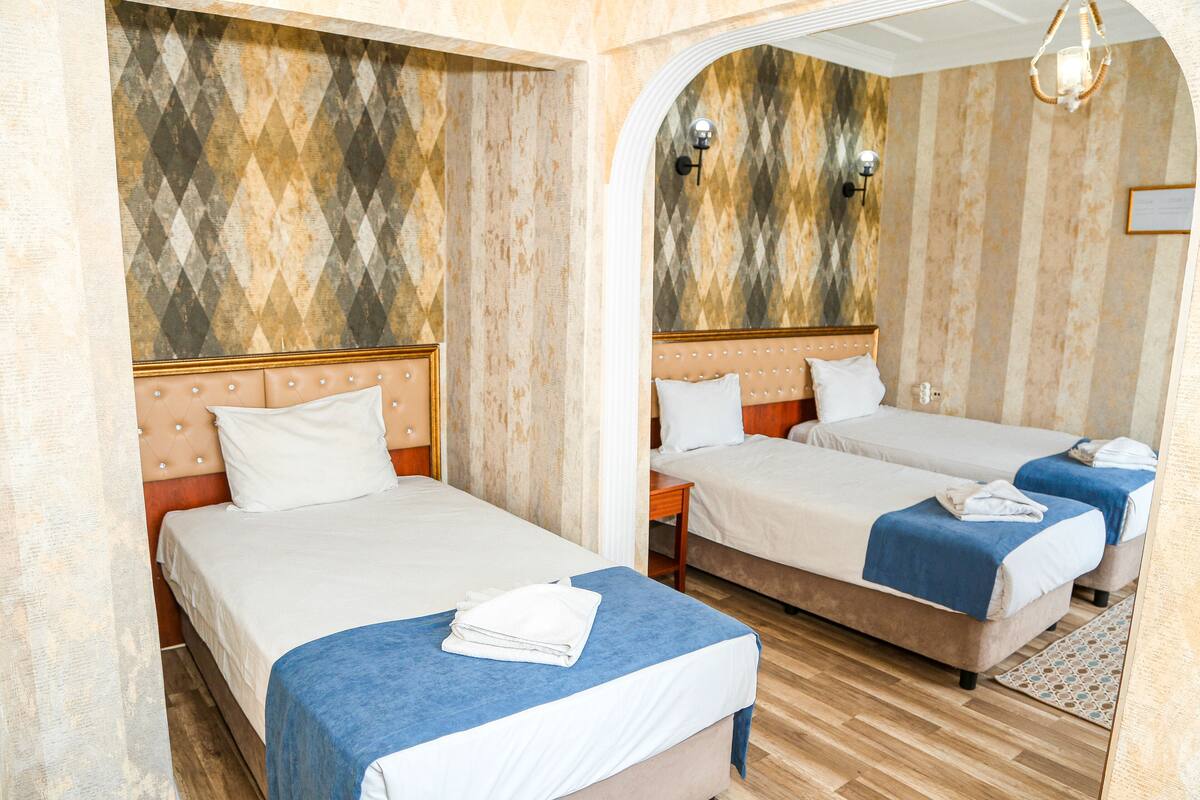 A hotel room with two beds, a wooden floor, and a patterned wall.