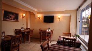 A dining area with wooden tables and chairs, a television mounted on the wall, and a painting on the wall.