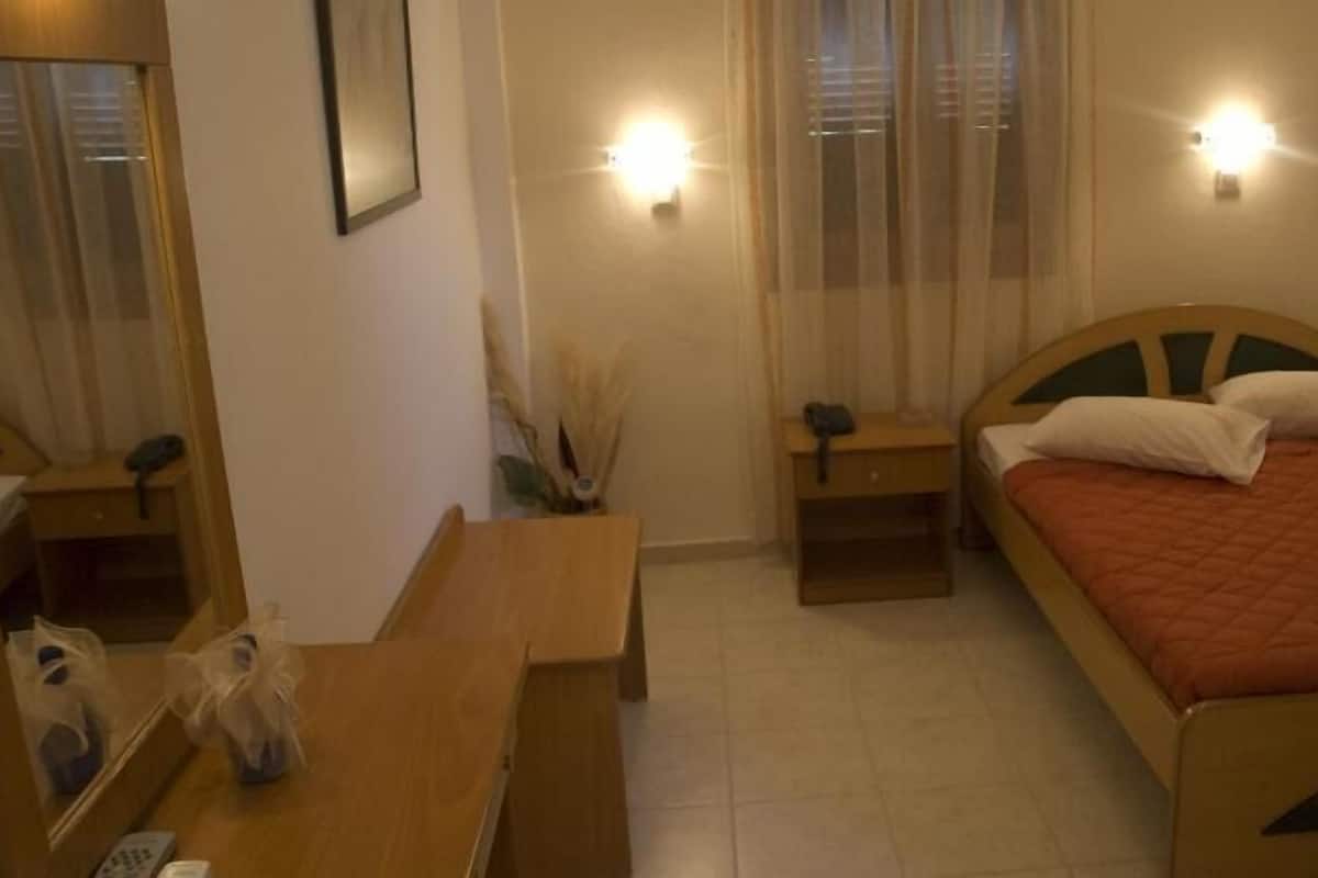 Quarto pequeno e acolhedor com cama, escrivaninha e cadeira. Há duas mesas de cabeceira com luminárias e um espelho na parede.
